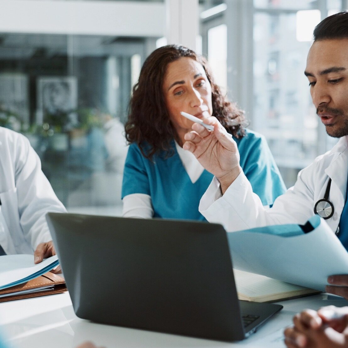 Doctor, nurse and laptop with discussion in clinic for healthcare treatment innovation or IRB approval report. Diversity, team or medical staff in hospital boardroom with paperwork for patient record.